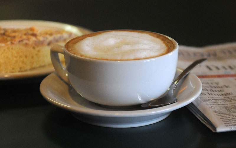 A Fika cappuccino sitting on a table with a pastry in the background.